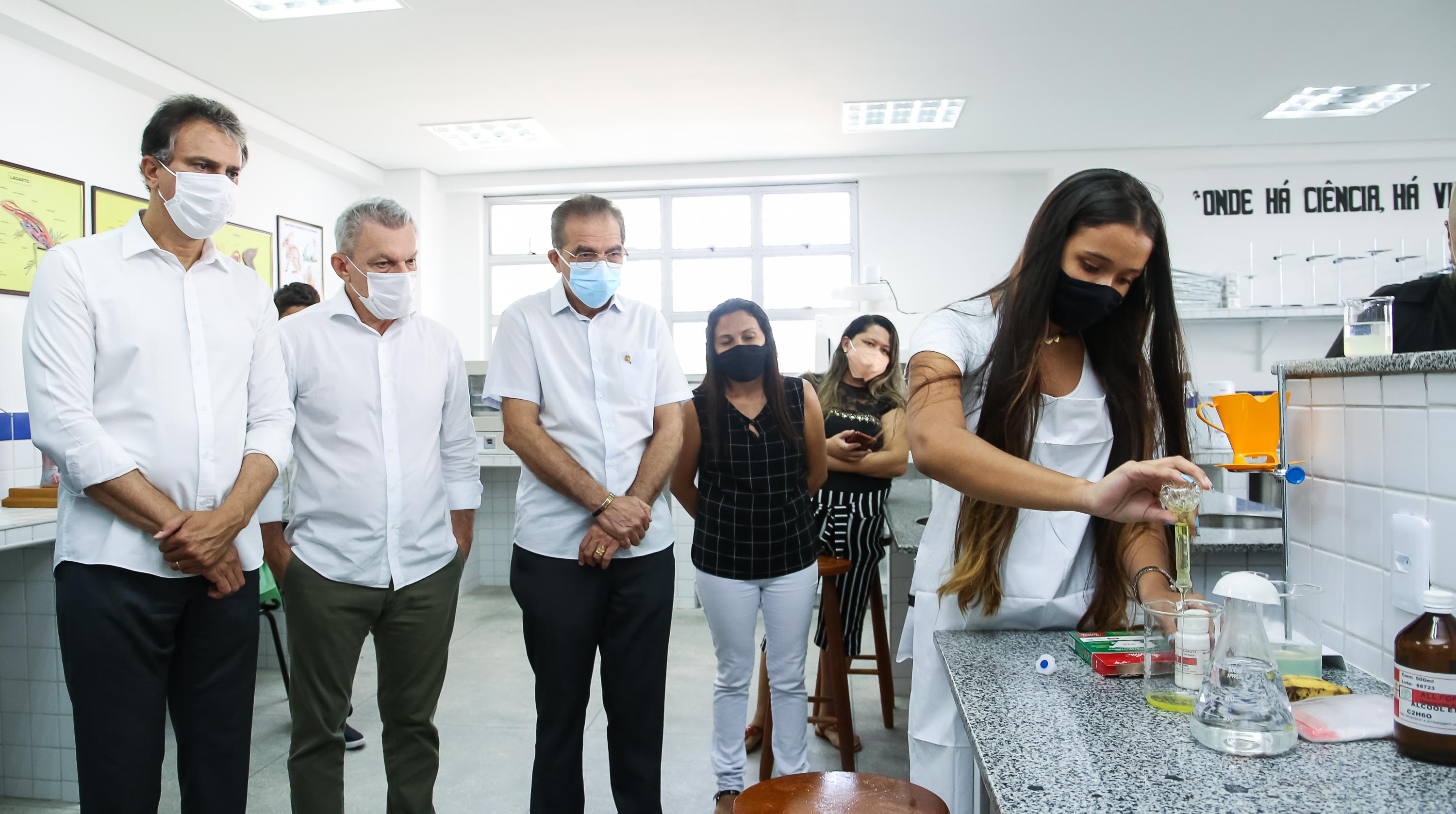 prefeito e governador observam uma aluna fazer um experimento químico dentro do laboratório da escola